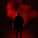 A mysterious silhouette standing against a backdrop of dramatic red smoke.